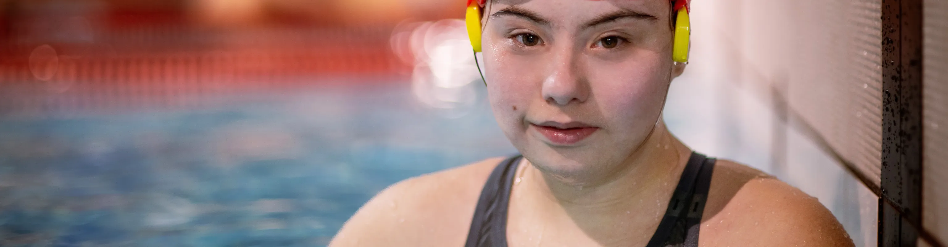 Girl with Downs Syndrome in a pool with swimming cap and goggles staring at camera
