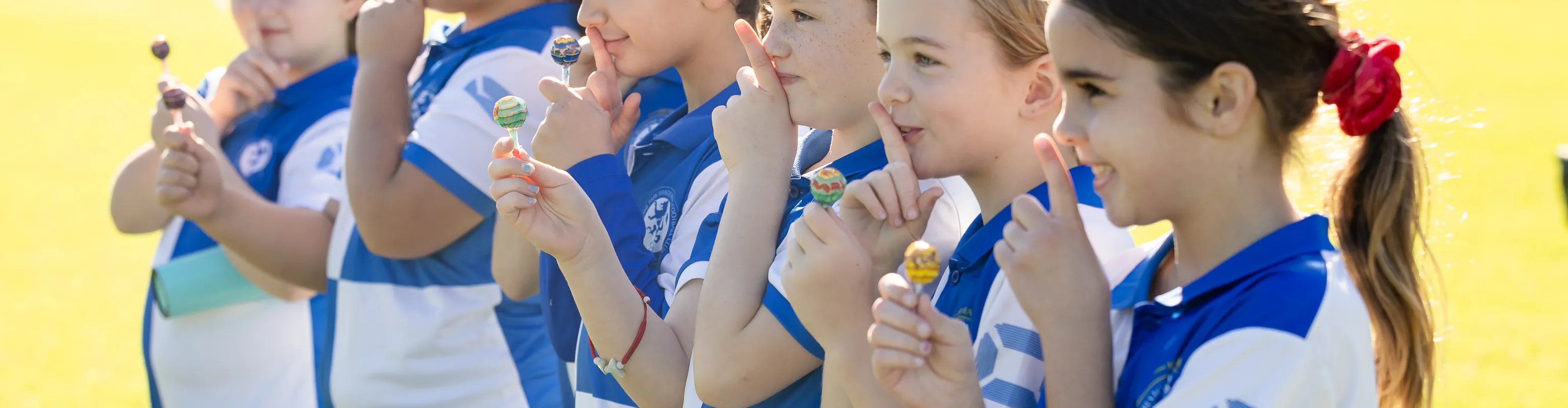 Girls in soccer kits doing 'shoosh' sign at sports field
