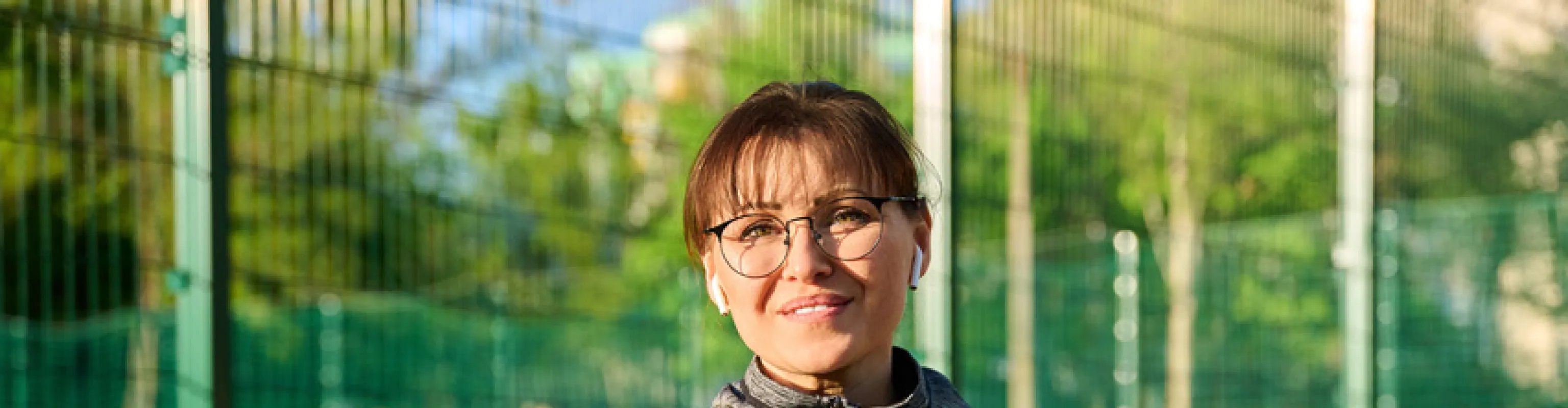 Woman smiling at a sports field holding a mobile phone