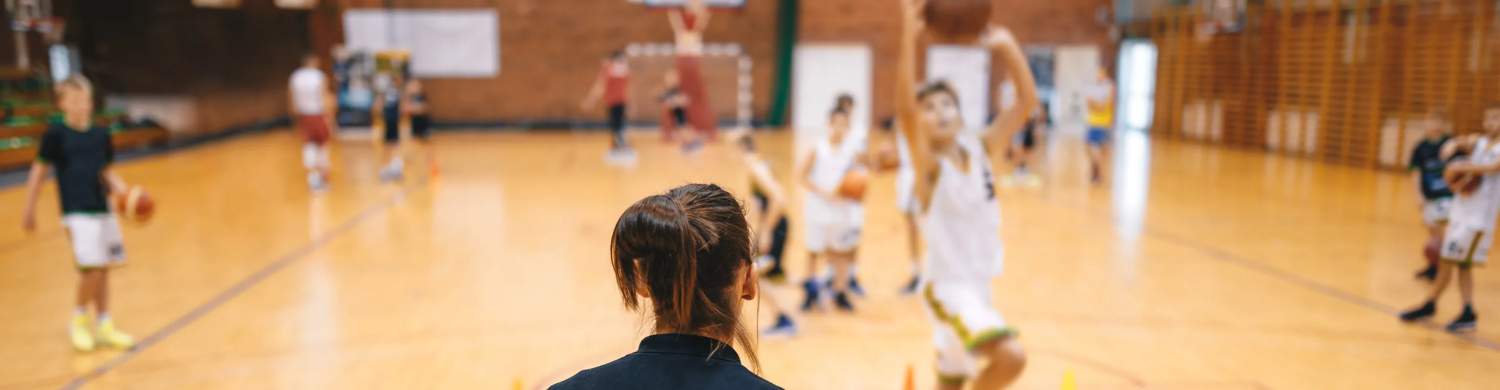 Basketball coach with back to camera running a drill with child athletes