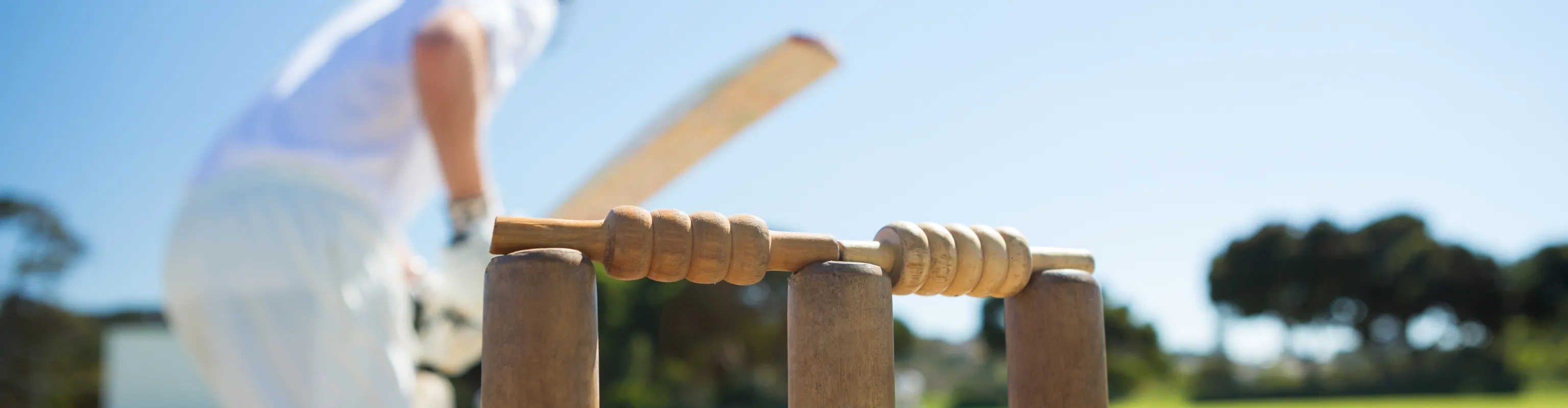 A man in whites plays a cricket shot, seen from behind the stumps