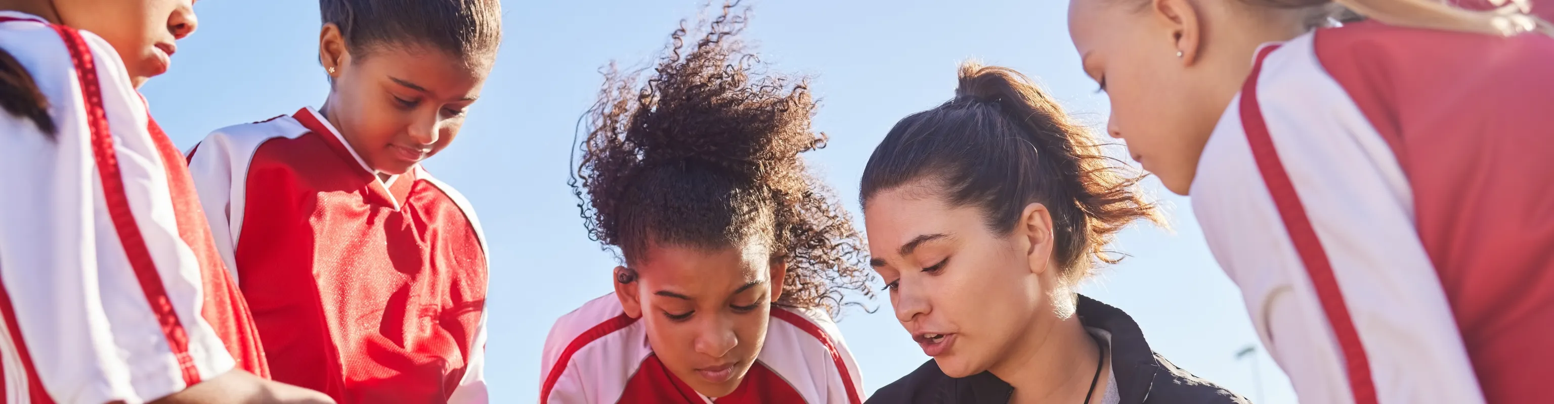 Junior football players surround their coach while she discusses what's on her clipboard.