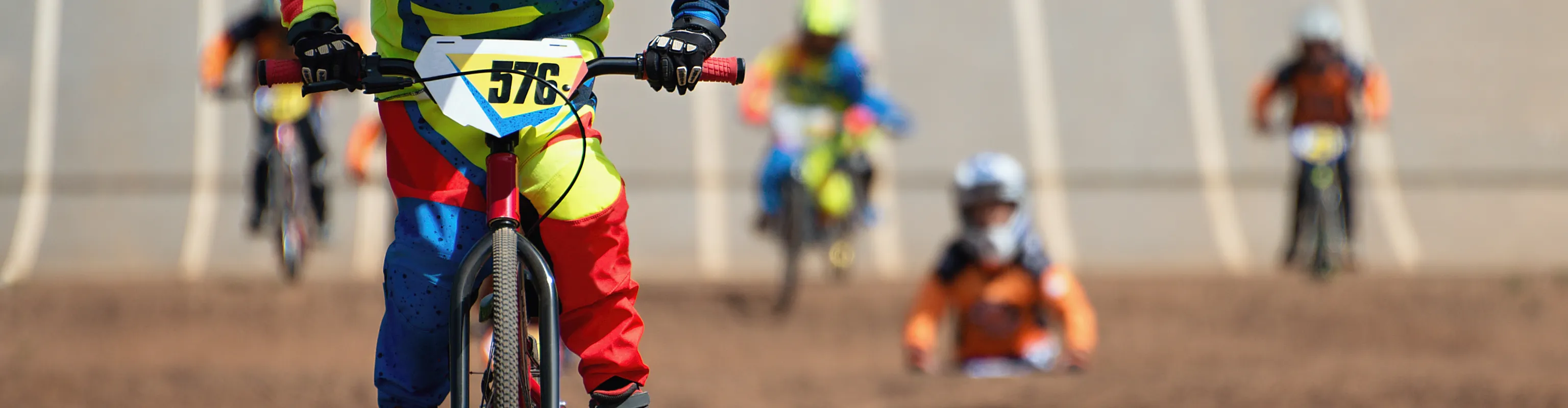 Kids in a BMX competition rush down the start gate and onto the track, towards the camera.