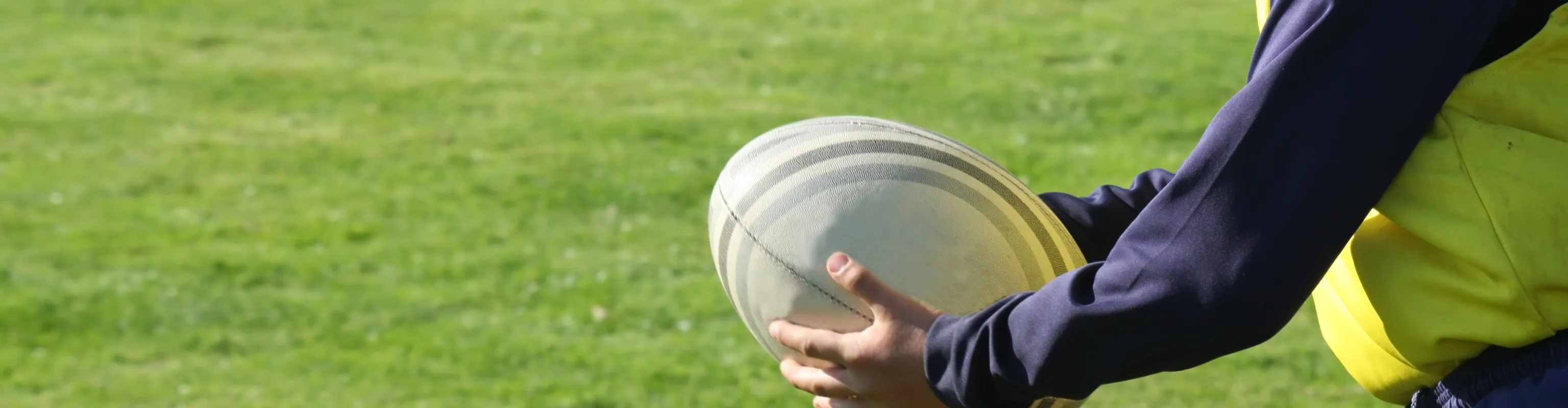 A boy holds a rugby ball during practice on a sunny, grassy playing field