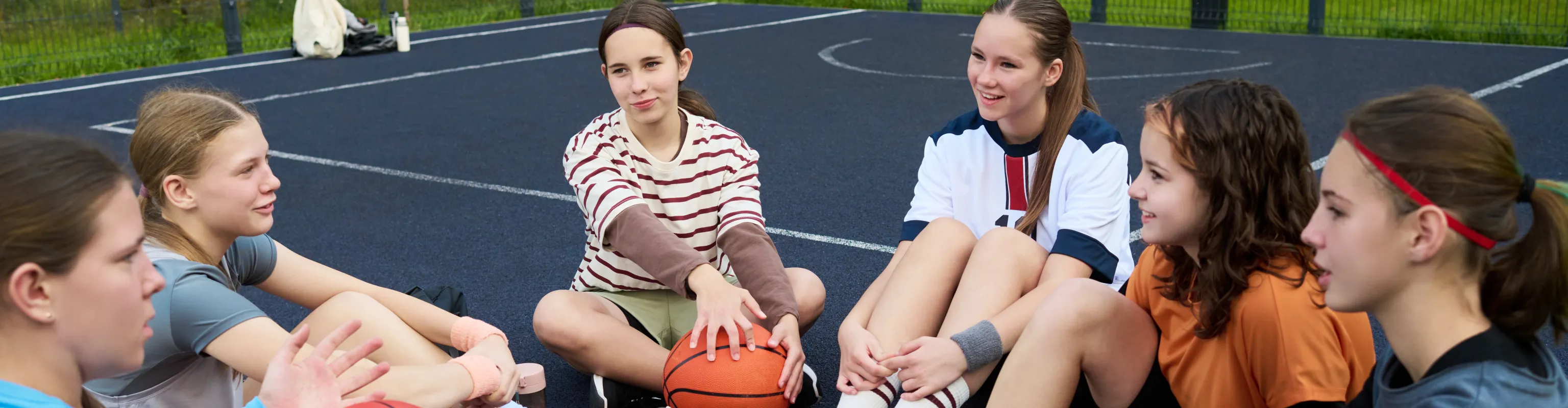 A group of teenagers sit on a basketball court and chat