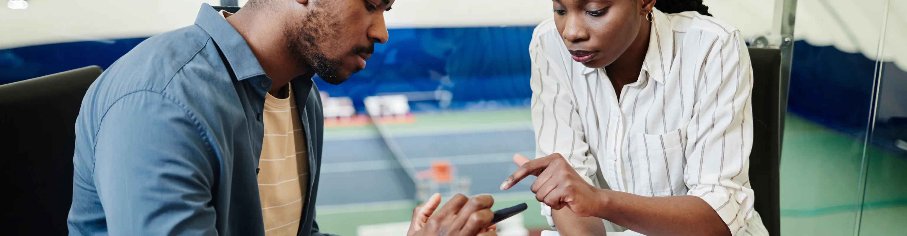 A tennis coach talks with her athlete as he reviews something on his phone