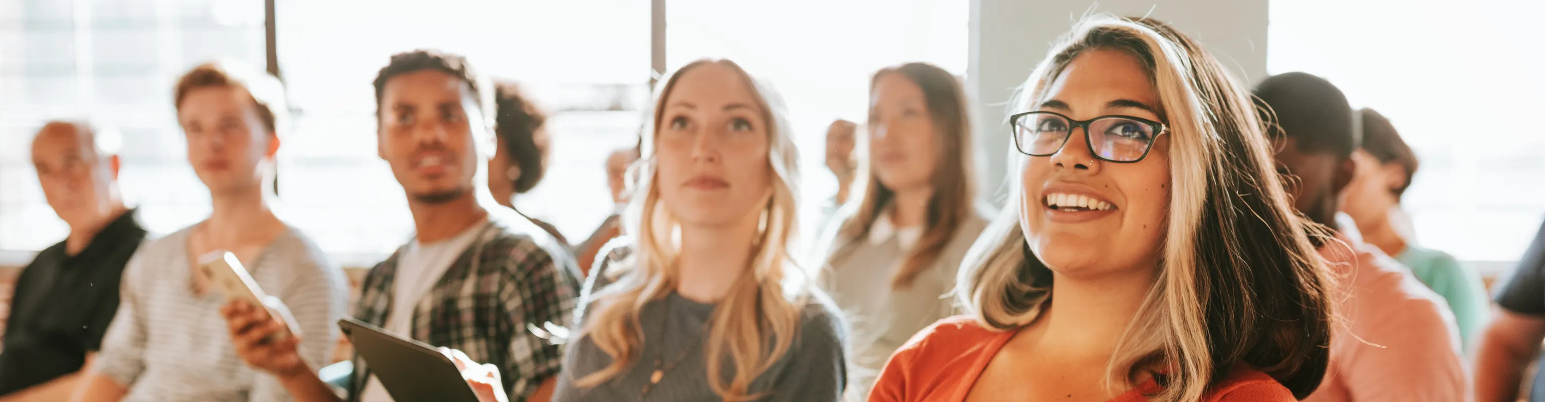 A group of people sit and listen attentively in a conference room arranged lecture-style