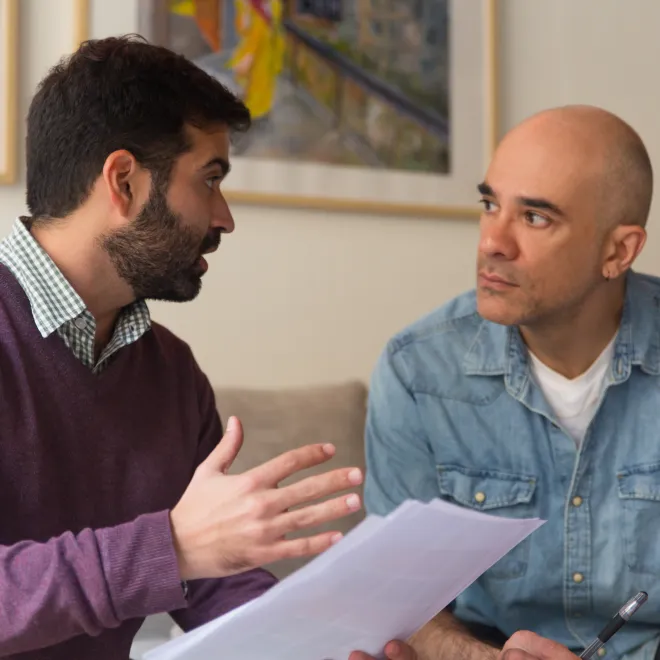 Two men with fair skin have a serious discussion on a couch