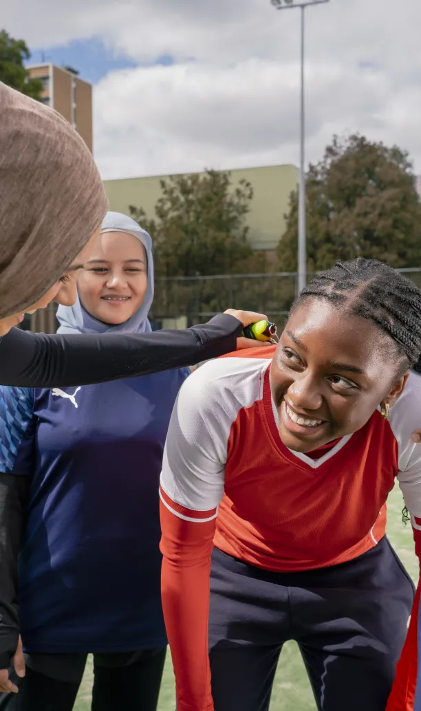 Four women share a laugh while resting during a friendly soccer match.