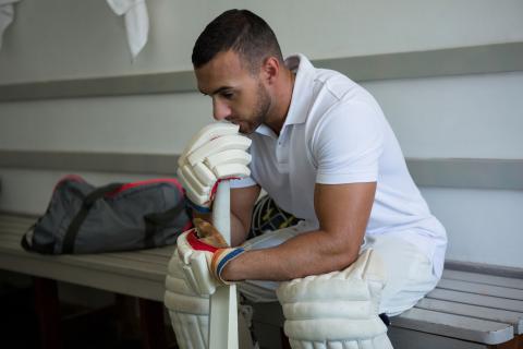 Man in cricket gear sitting in change rooms