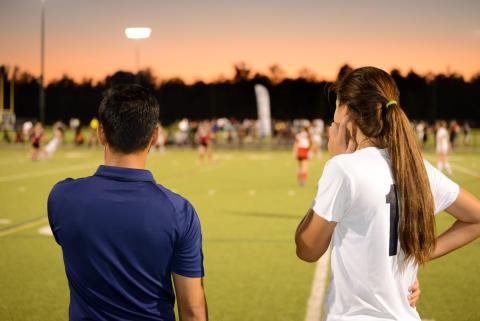 Man and girl watching sporting match on the sidelines at night
