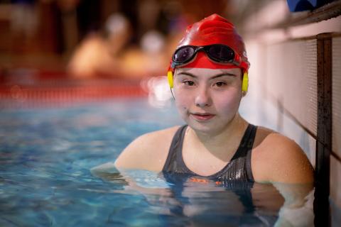 Girl with Downs Syndrome in a pool with swimming cap and goggles staring at camera