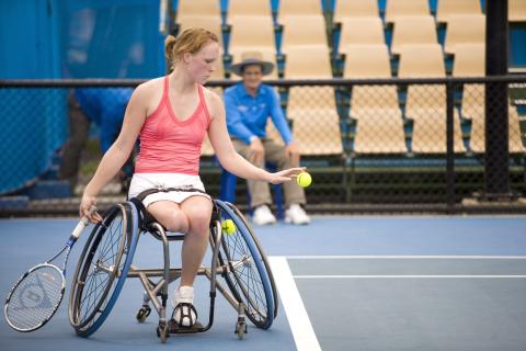 Woman in wheelchair serving a tennis ball