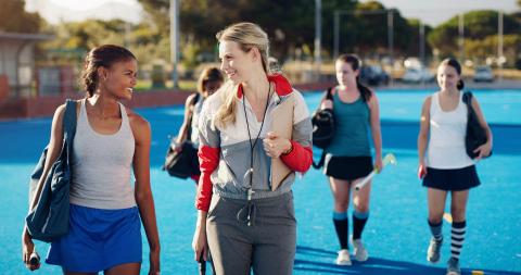 Smiling field hockey players walk with their coach after a training session