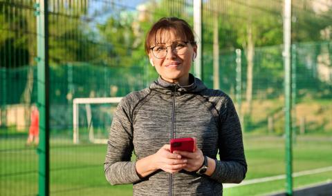 Woman smiling at a sports field holding a mobile phone