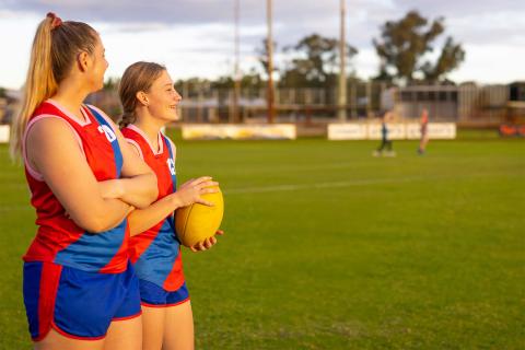 Two young women dressed in red and blu Australian football jerseys