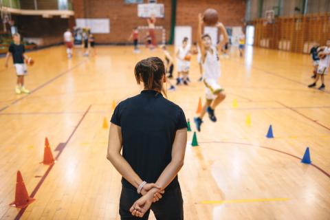 Basketball coach with back to camera running a drill with child athletes