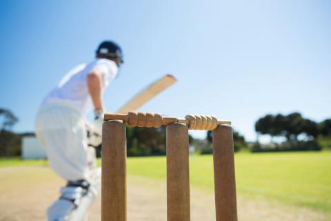 A man in whites plays a cricket shot, seen from behind the stumps