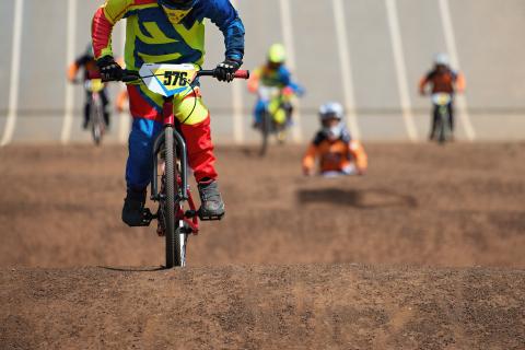 Kids in a BMX competition rush down the start gate and onto the track, towards the camera.
