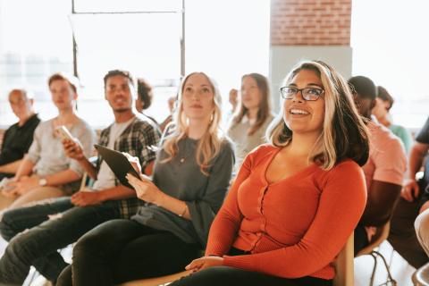A group of people sit and listen attentively in a conference room arranged lecture-style