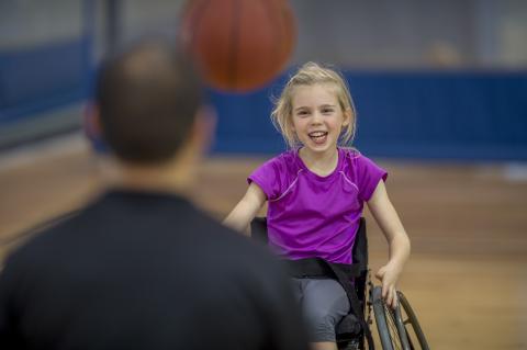 Young girl in a wheelchair throwing a basketball to a man