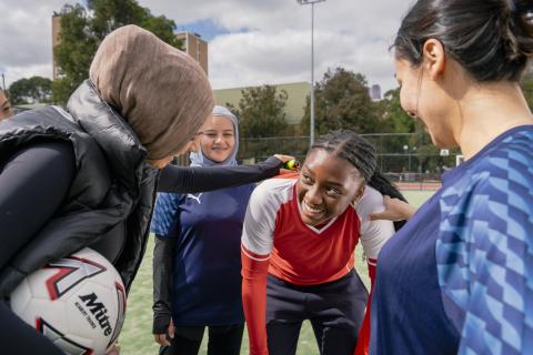 Four women share a laugh while resting during a friendly soccer match.