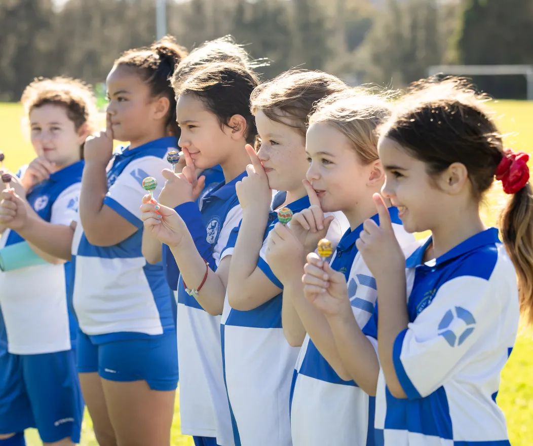 Girls in soccer kits doing 'shoosh' sign at sports field