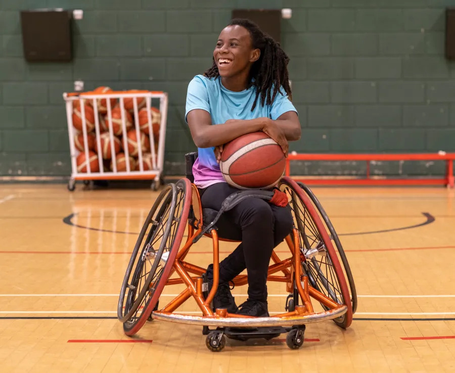 Woman in a wheelchair smiling and holding a basketball