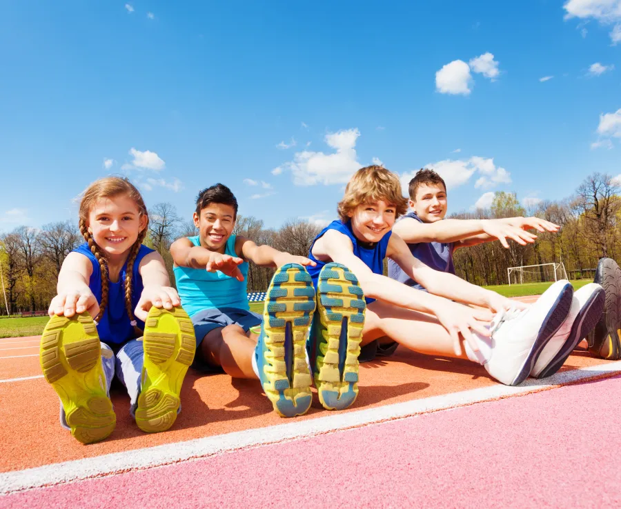 Kids in athletics gear stretching on an athletics track