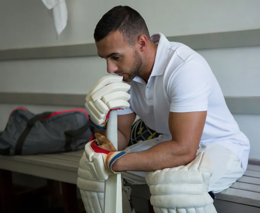Man in cricket gear sitting in change rooms