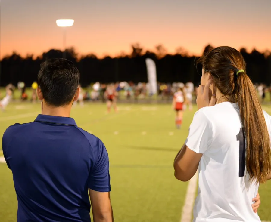 Man and girl watching sporting match on the sidelines at night