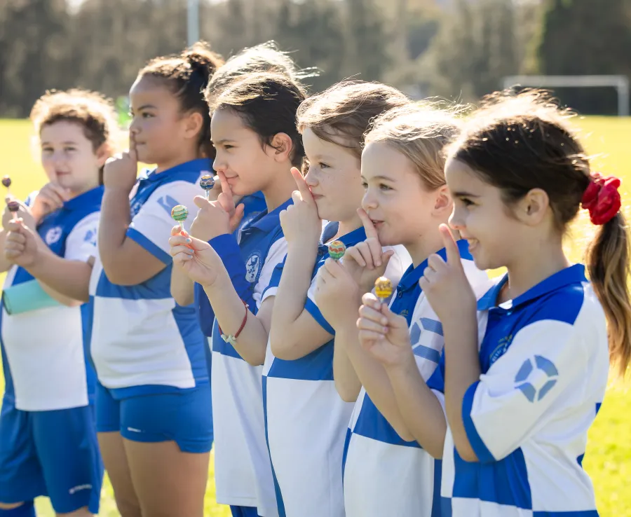 Girls in soccer kits doing 'shoosh' sign at sports field