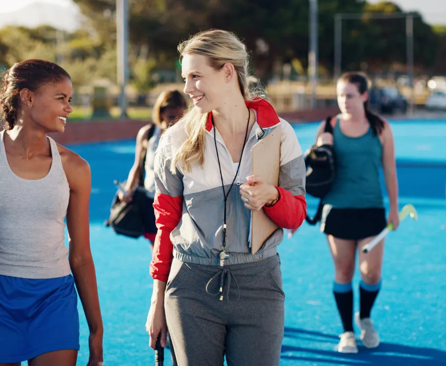 Smiling field hockey players walk with their coach after a training session