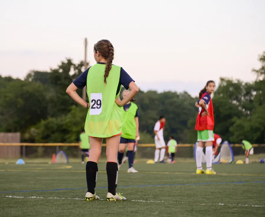 Teenage girls at football training stand on the playing field waiting for instruction
