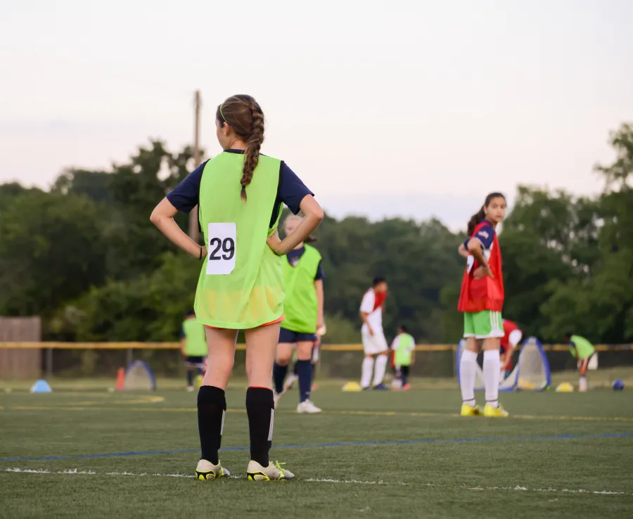 Teenage girls at football training stand on the playing field waiting for instruction