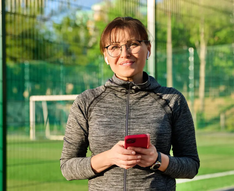 Woman smiling at a sports field holding a mobile phone