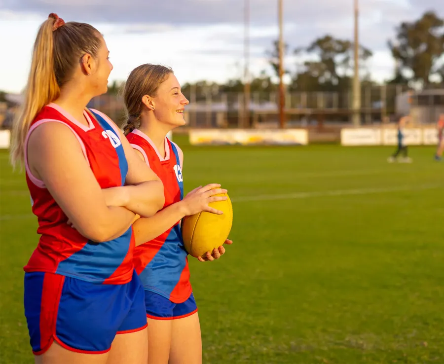 Two young women dressed in red and blu Australian football jerseys