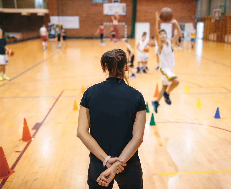 Basketball coach with back to camera running a drill with child athletes