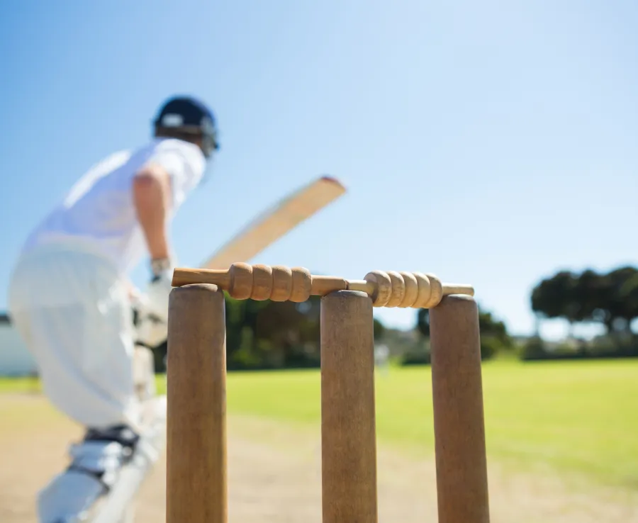 A man in whites plays a cricket shot, seen from behind the stumps
