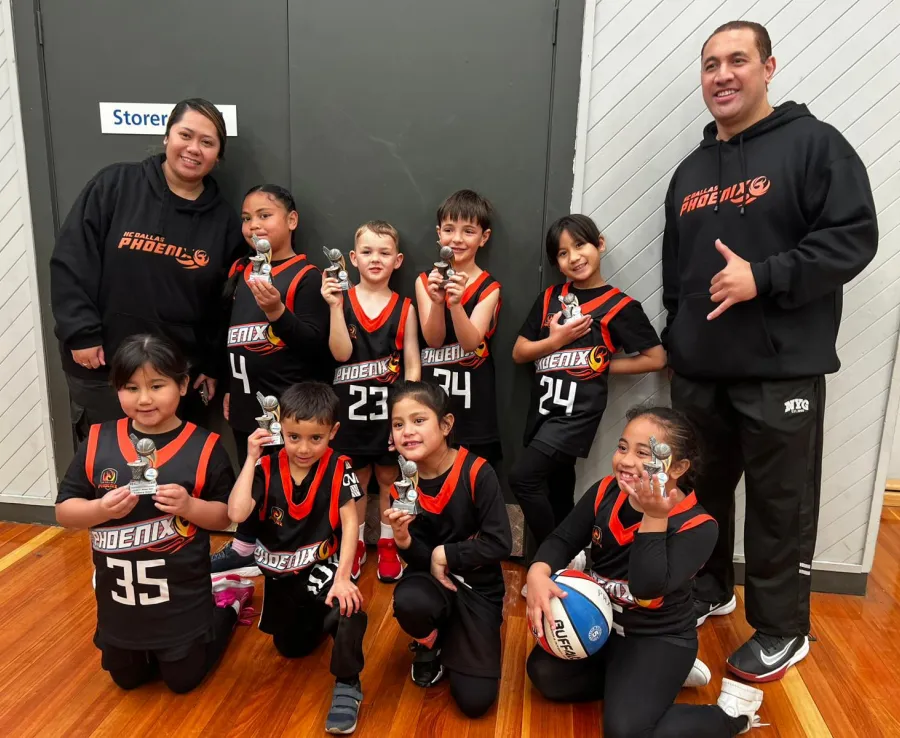 A team of junior Phoenix players pose with medals, flanked by their coaches, one of which is throwing a shaka