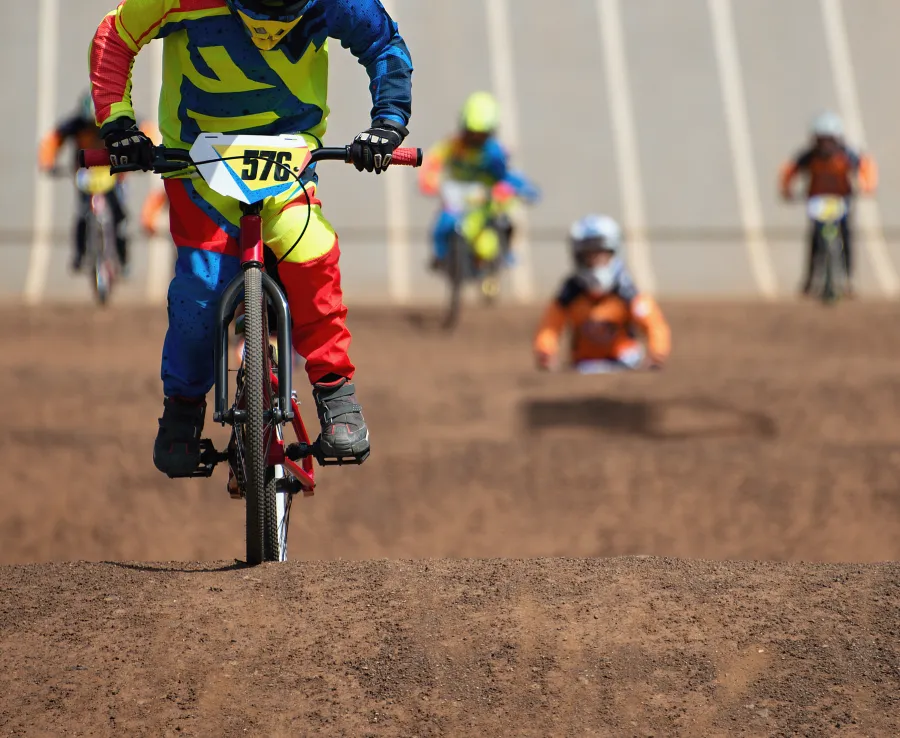 Kids in a BMX competition rush down the start gate and onto the track, towards the camera.