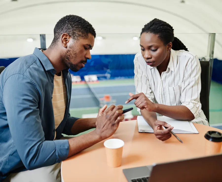 A tennis coach talks with her athlete as he reviews something on his phone