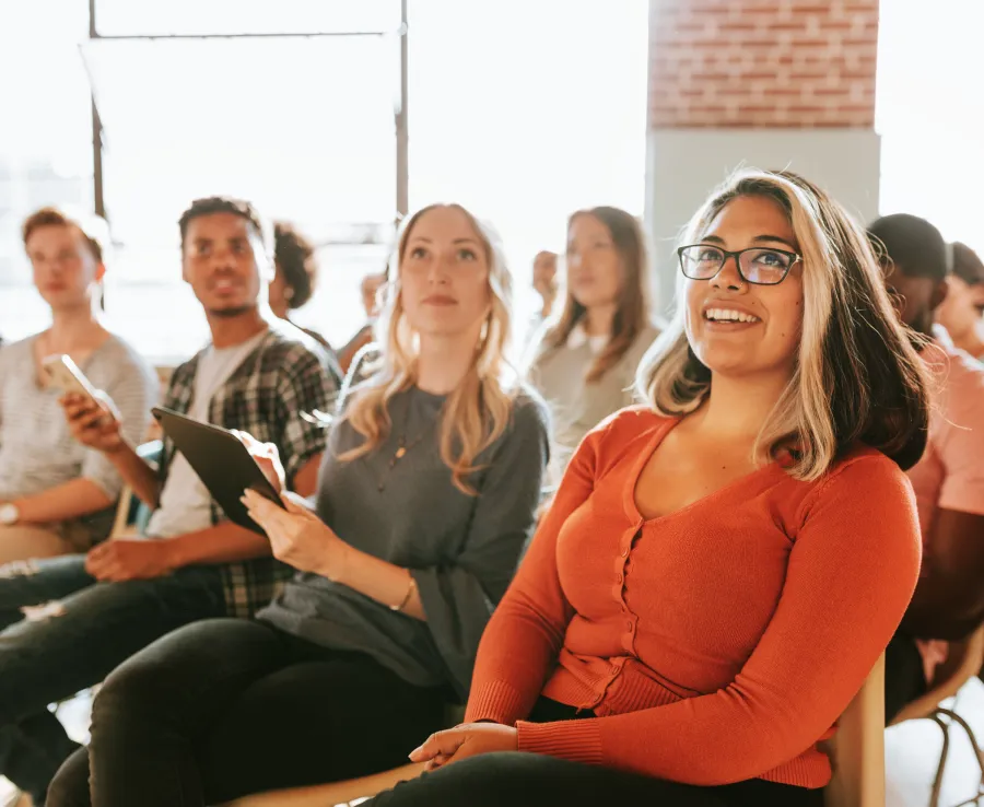A group of people sit and listen attentively in a conference room arranged lecture-style