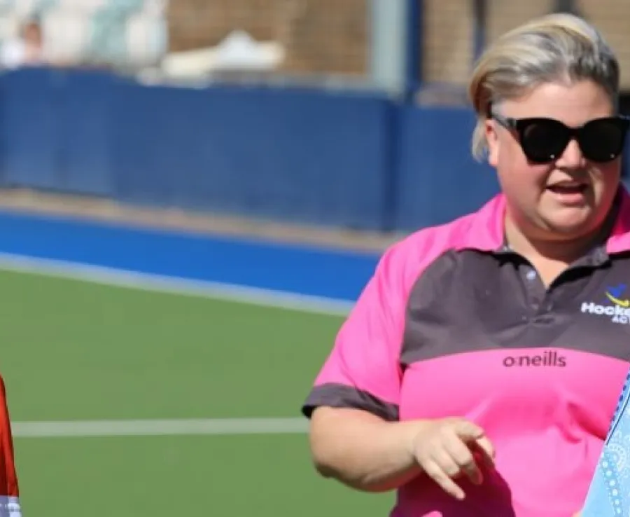 A match official talks to to a junior official as a girl wearing an 'umpire in training' polo shirt