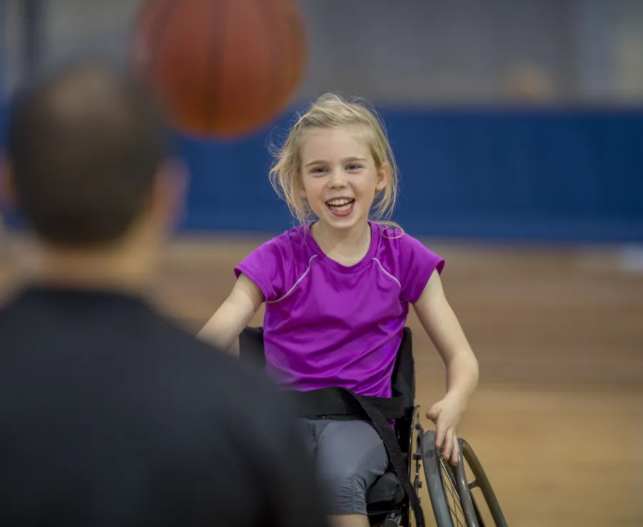 Young girl in a wheelchair throwing a basketball to a man