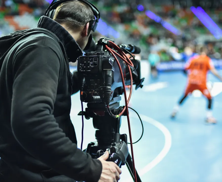 Man in black outfit films an indoor sport game